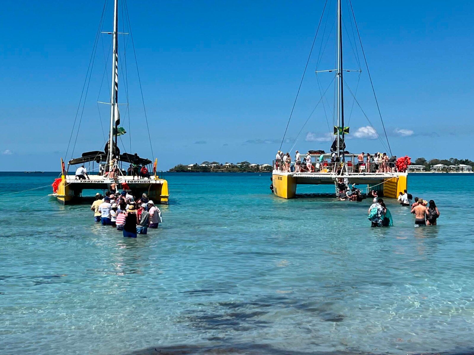 Two catamarans anchored in shallow water, participants boarding from the beach in Negril Two catamarans anchored in shallow water, participants boarding from the beach in Negril