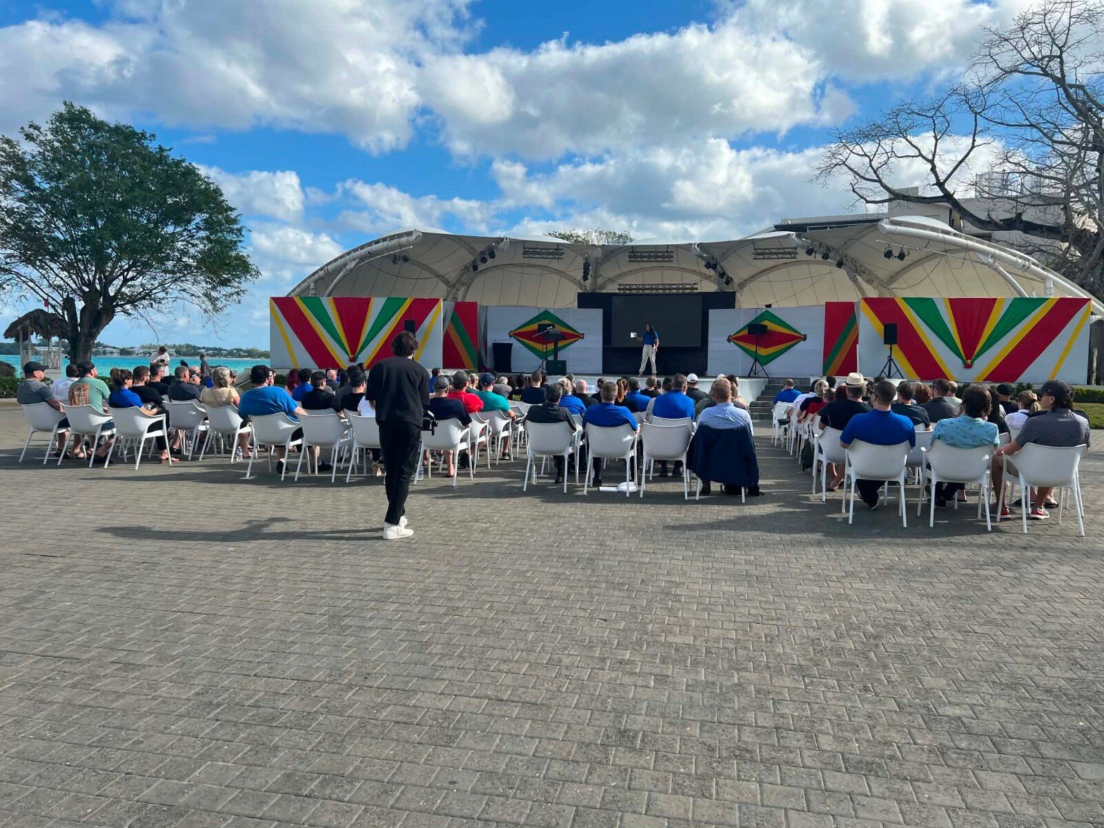 Participants seated facing the stage during an outdoor conference session Participants seated facing the stage during an outdoor conference session