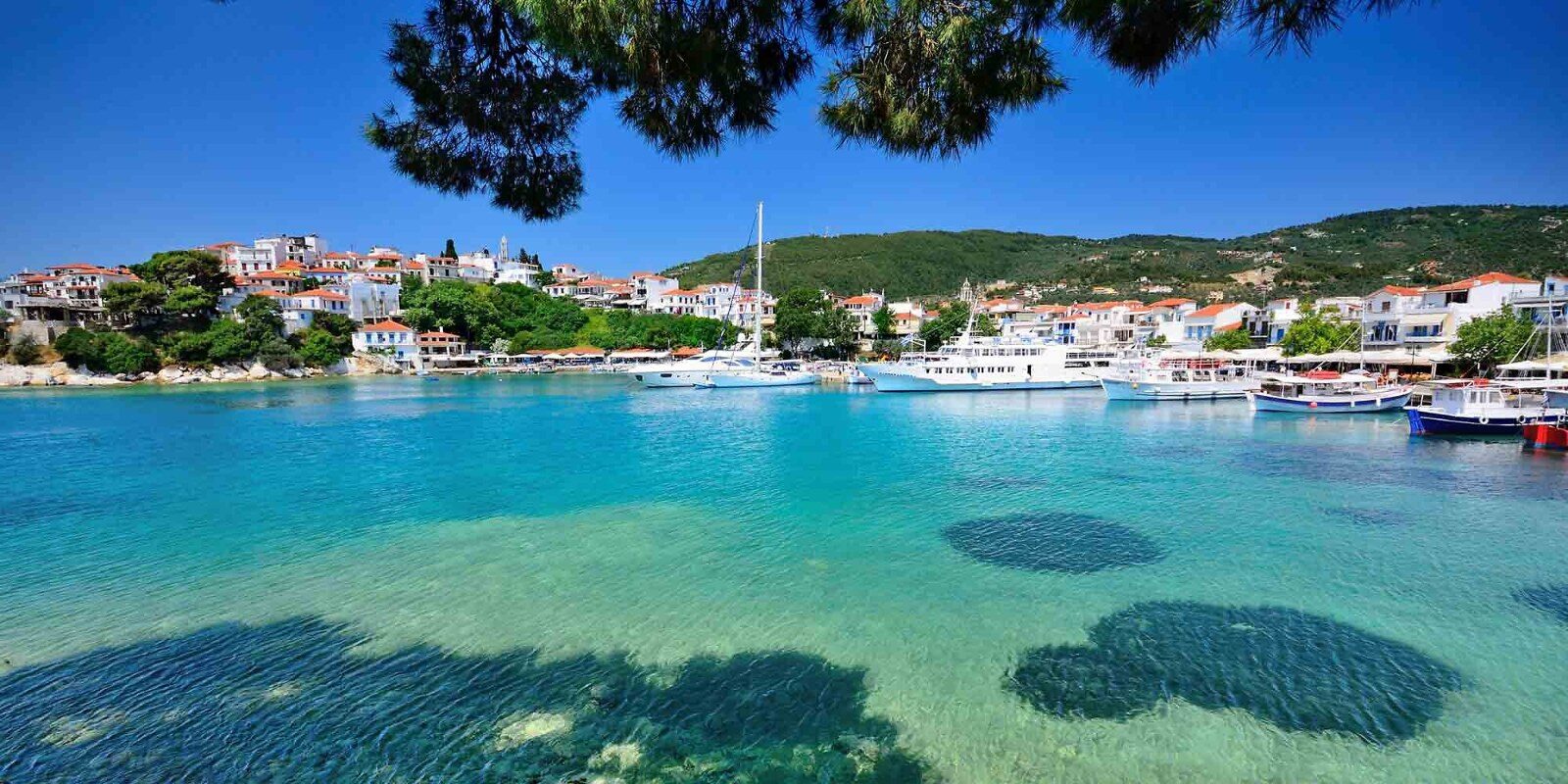 A Greek harbour with turquoise water surrounded by hills A Greek harbour with turquoise water surrounded by hills