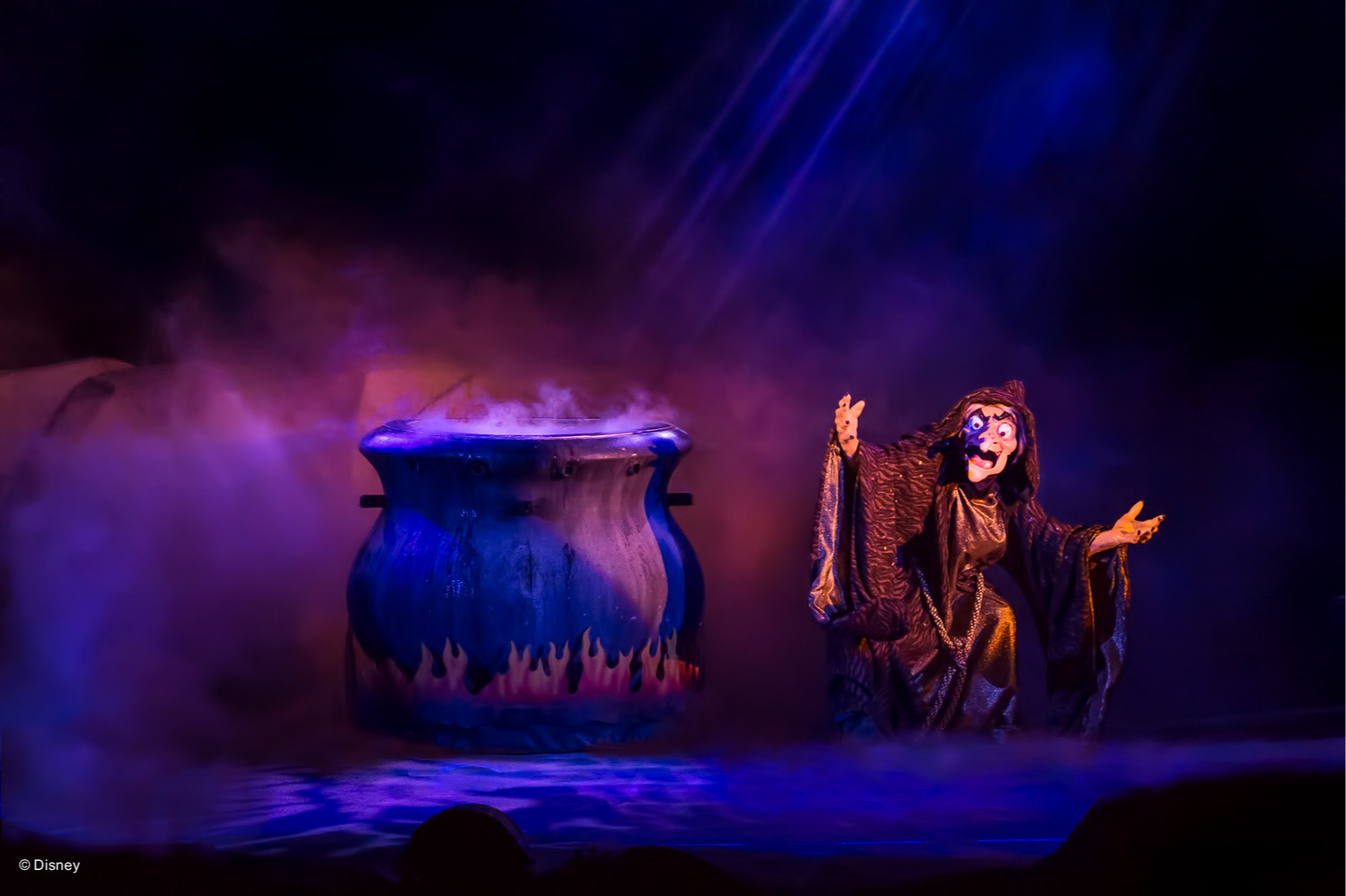 The witch from Snow White, arms outstretched beside a giant cauldron in purple smoke, during the Fantasmic show, at Disney’s Hollywood Studios The witch from Snow White, arms outstretched beside a giant cauldron in purple smoke, during the Fantasmic show, at Disney’s Hollywood Studios
