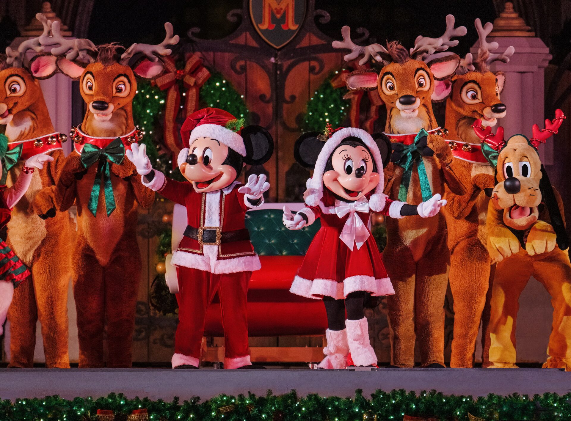 Mickey and Minnie in Santa outfits wave from a sleigh surrounded by costumed reindeer, on a garland-trimmed stage, at Magic Kingdom Mickey and Minnie in Santa outfits wave from a sleigh surrounded by costumed reindeer, on a garland-trimmed stage, at Magic Kingdom
