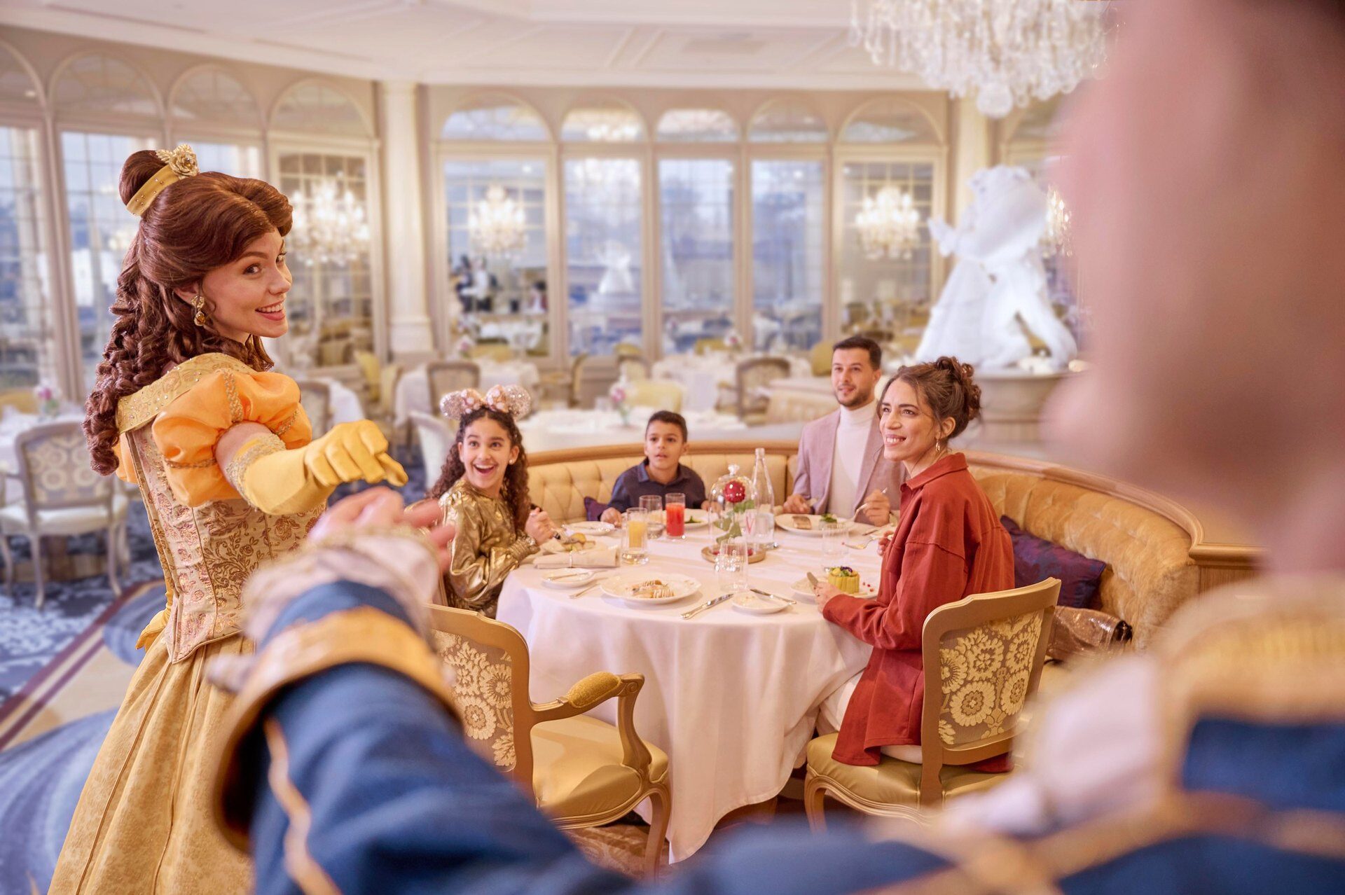 Belle, de La Belle et la Bête, salue une famille attablée dans une salle à manger lumineuse du Disneyland Hotel. Photo : ©Disney.