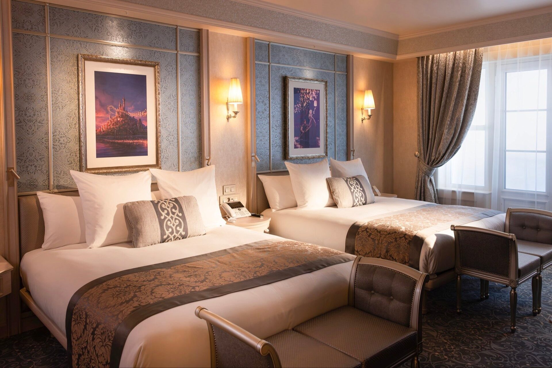 Une chambre Supérieure du Disneyland Hotel à Disneyland Paris, avec deux grands lits, des tons bleu et or et des œuvres d'art Disney au-dessus des têtes de lit. Photo : ©Disney.