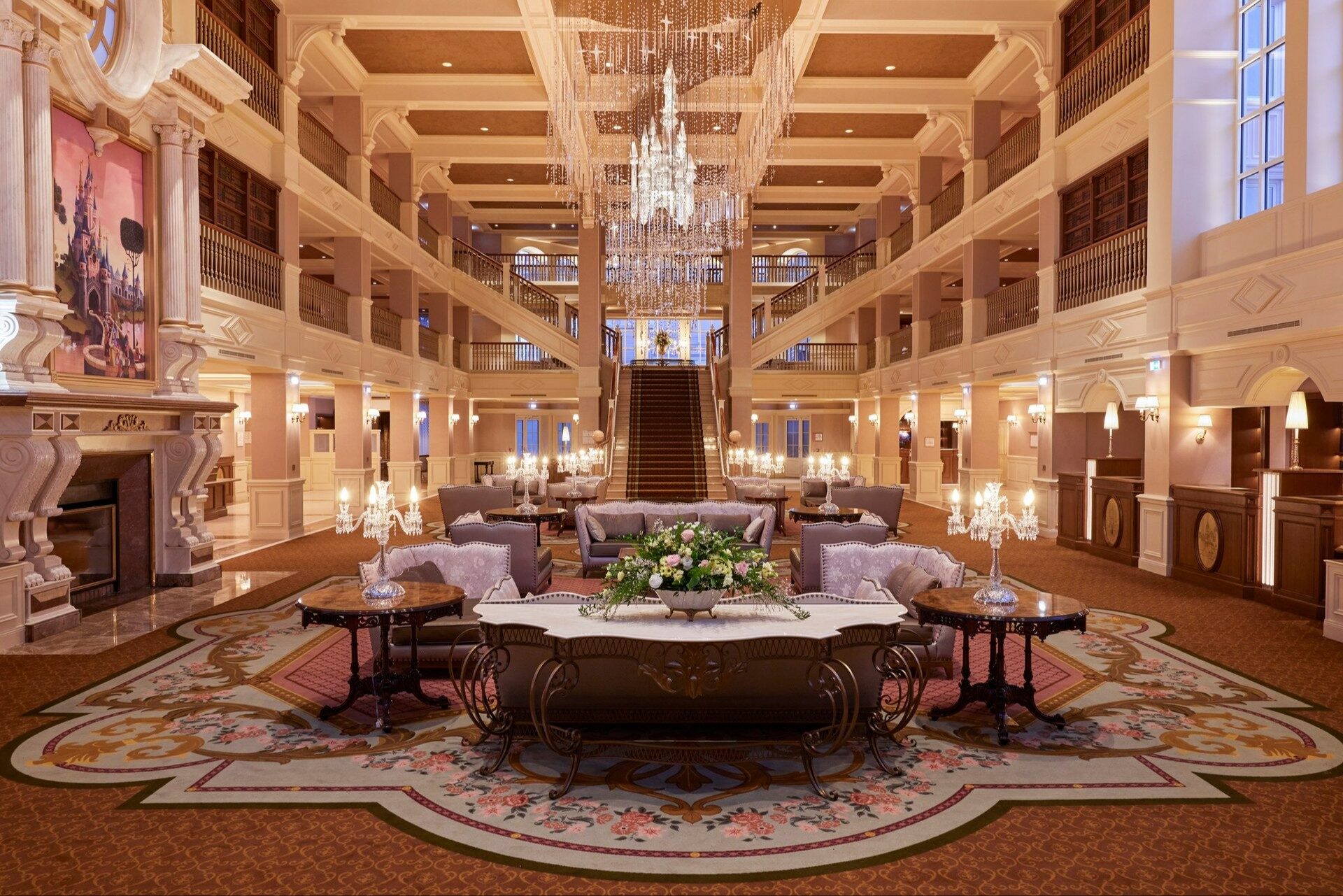 Le grand hall du Disneyland Hotel à Disneyland Paris, avec ses lustres de cristal, ses balcons sur plusieurs étages et son escalier central. Photo : ©Disney.