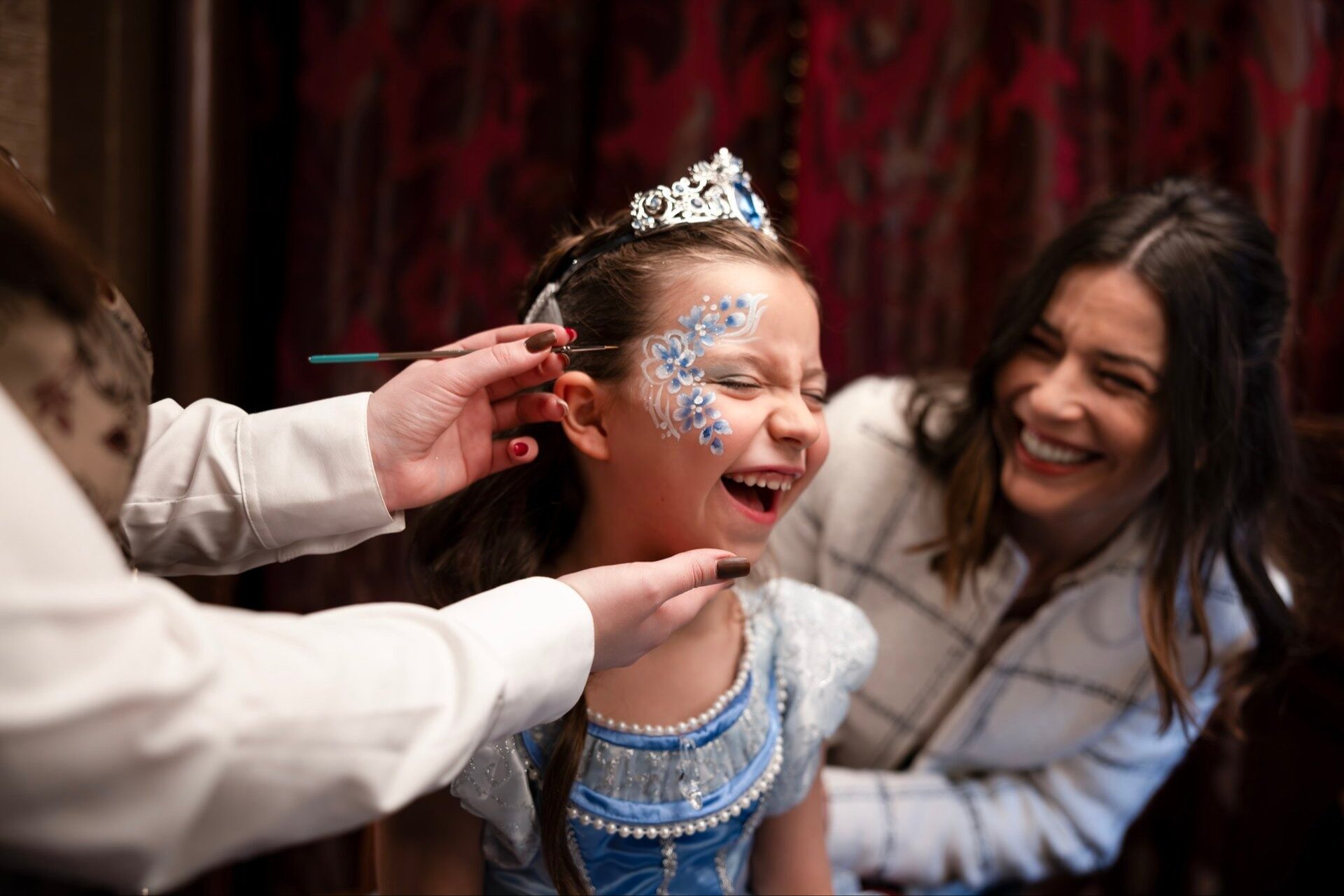 A little girl in a princess gown laughs as her face is painted during her royal makeover at Disneyland Hotel.