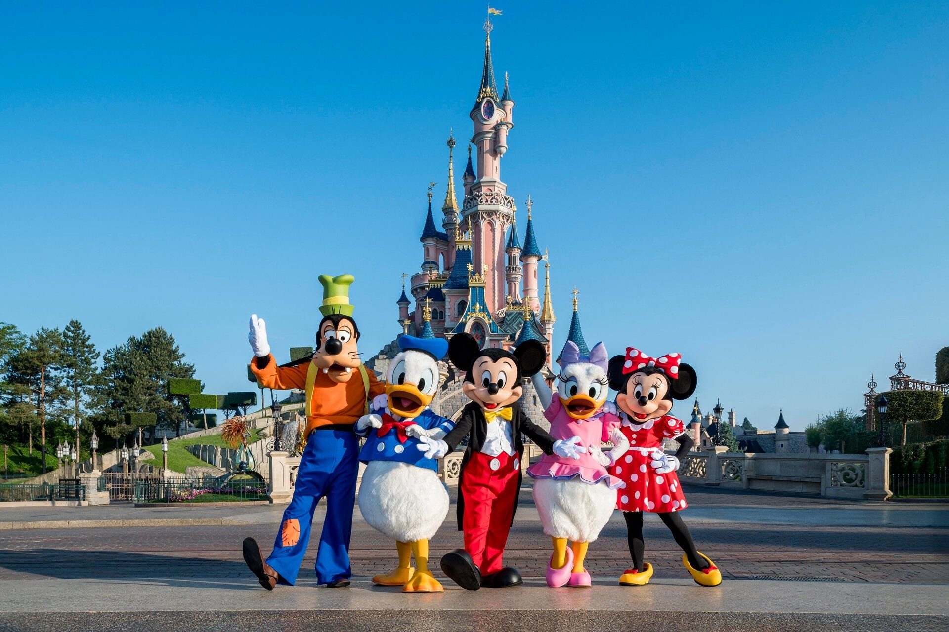 Goofy, Donald, Mickey, Daisy and Minnie in front of Sleeping Beauty Castle in Disneyland Park under a blue sky. Photo: ©Disney.