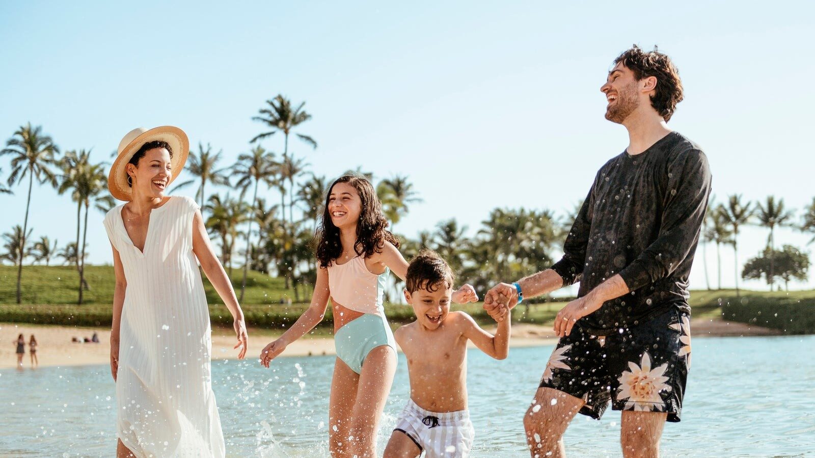Une famille marche dans l'eau du lagon de Ko Olina, devant Aulani, A Disney Resort & Spa Une famille marche dans l'eau du lagon de Ko Olina, devant Aulani, A Disney Resort & Spa