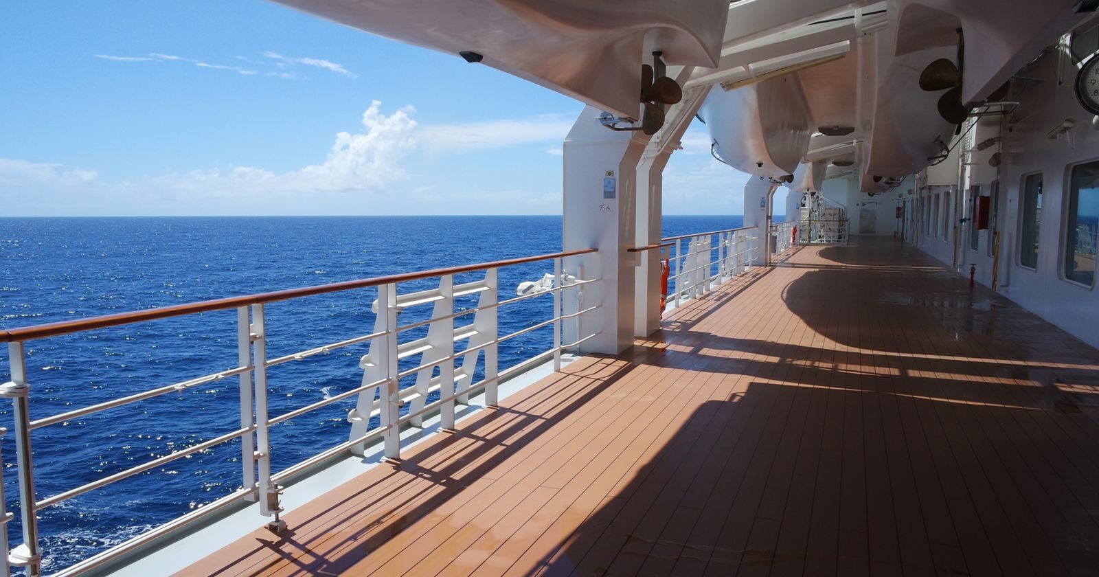 Open cruise ship deck with lifeboats and railings overlooking blue ocean water