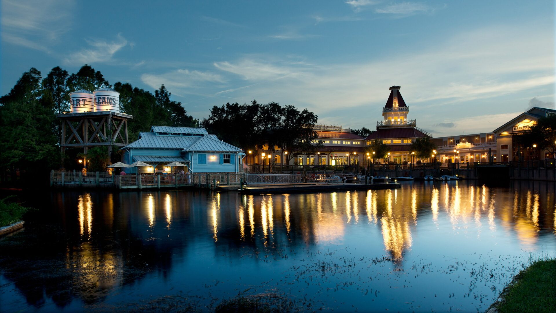 The lit buildings of Disney’s Port Orleans Resort – Riverside reflected in the river at dusk, the water tower on the left The lit buildings of Disney’s Port Orleans Resort – Riverside reflected in the river at dusk, the water tower on the left
